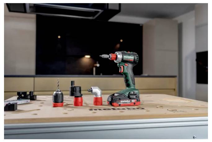 Kabelloses Metabo-Bohrgerät auf einer Werkbank stehend mit drei Bohraufsätzen in einer Werkstatt-Küchen-Umgebung.