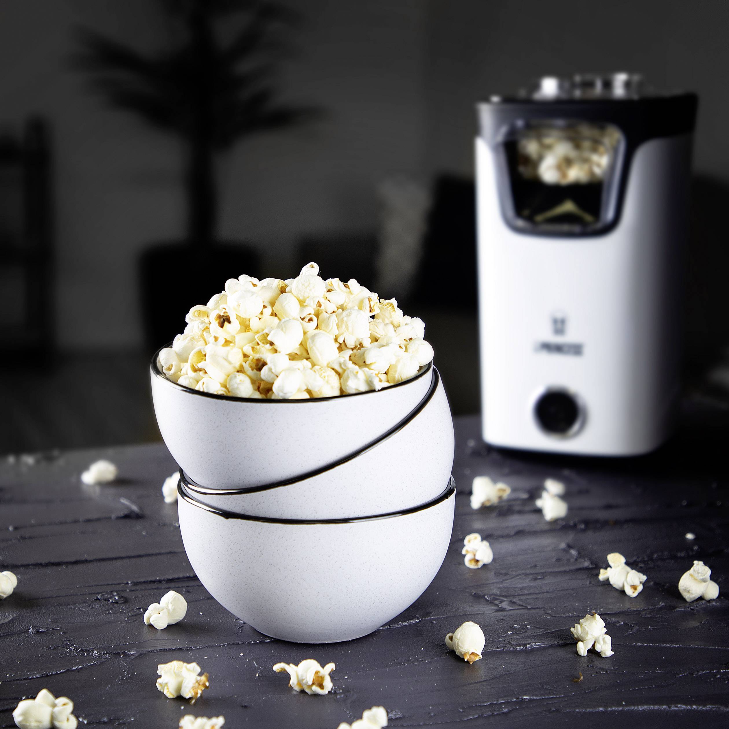 Schüssel mit frischem Popcorn steht auf einem Tisch, im Hintergrund eine Popcornmaschine.