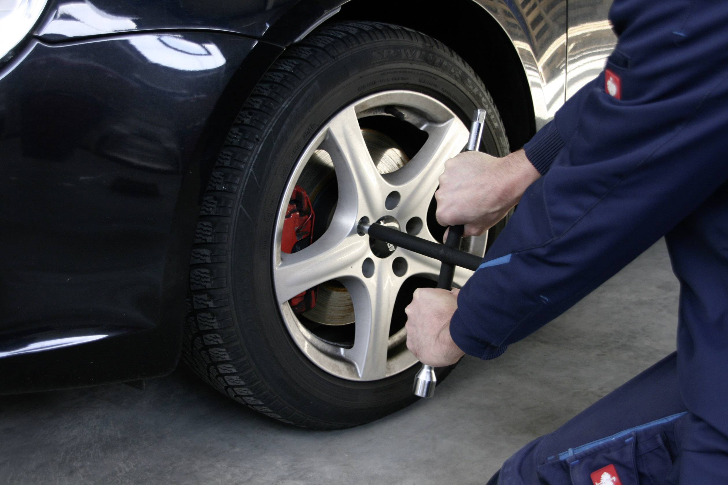 Eine Person wechselt einen Autoreifen, indem sie die Radmutter mit einem Radkreuzschlüssel anzieht.