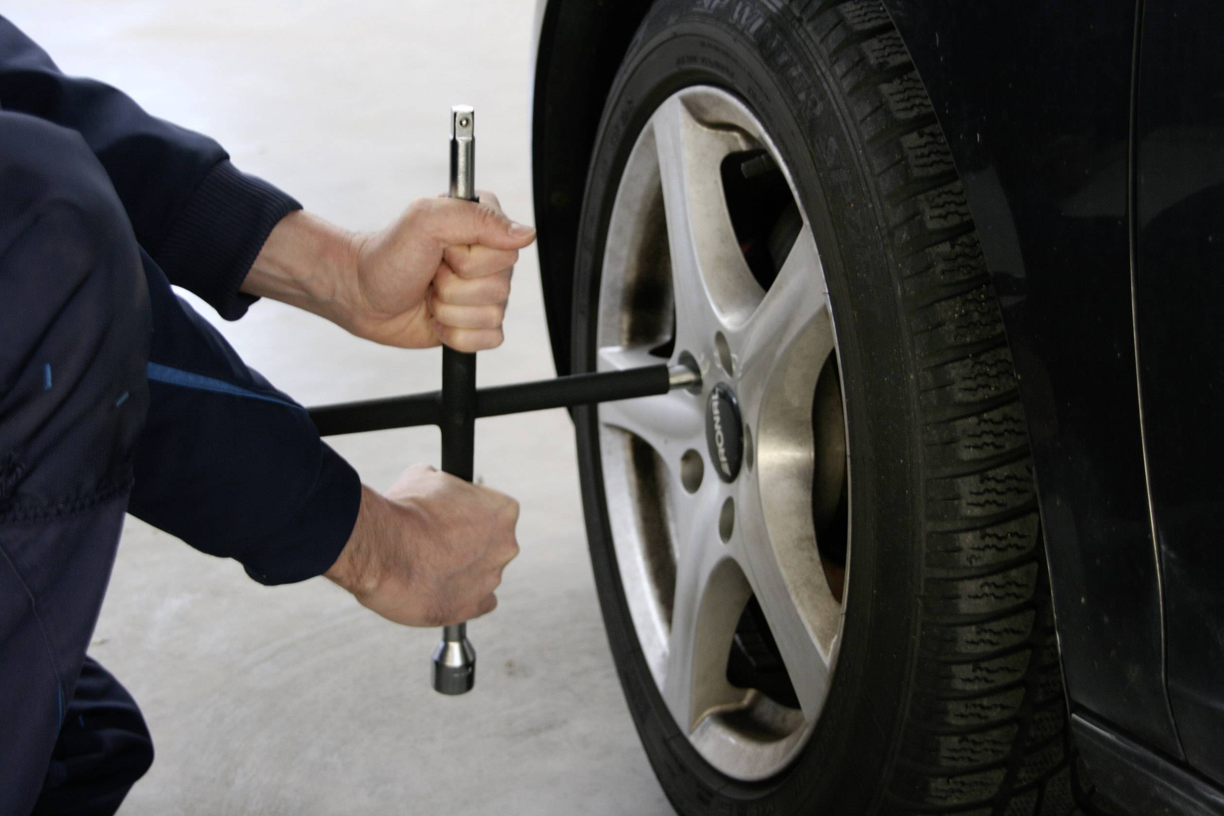 Eine Person wechselt einen Autoreifen. Sie verwenden einen Radschlüssel, um die Radmuttern zu lösen.