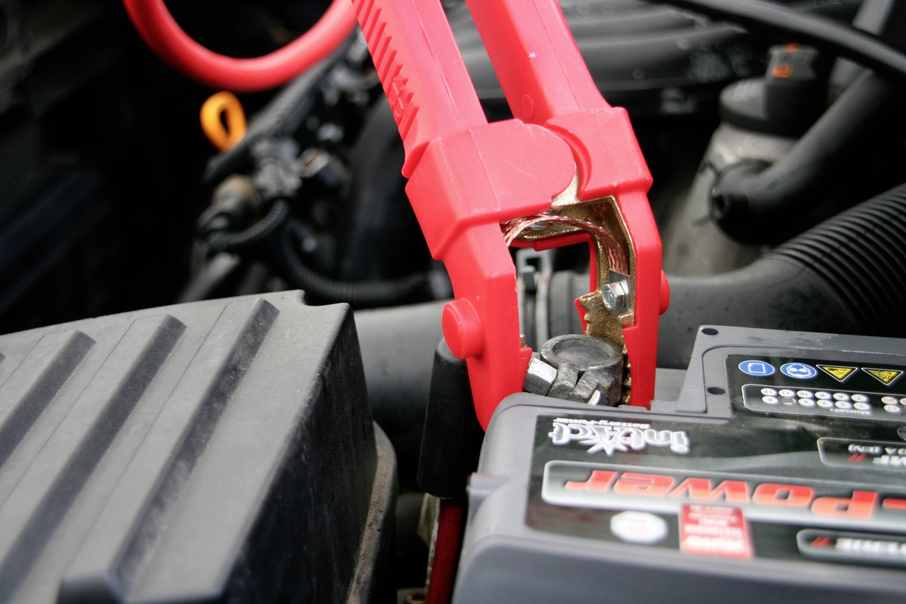 Eine rote Starthilfezange ist an die Autobatterie angeschlossen, um das Fahrzeug zu starten.