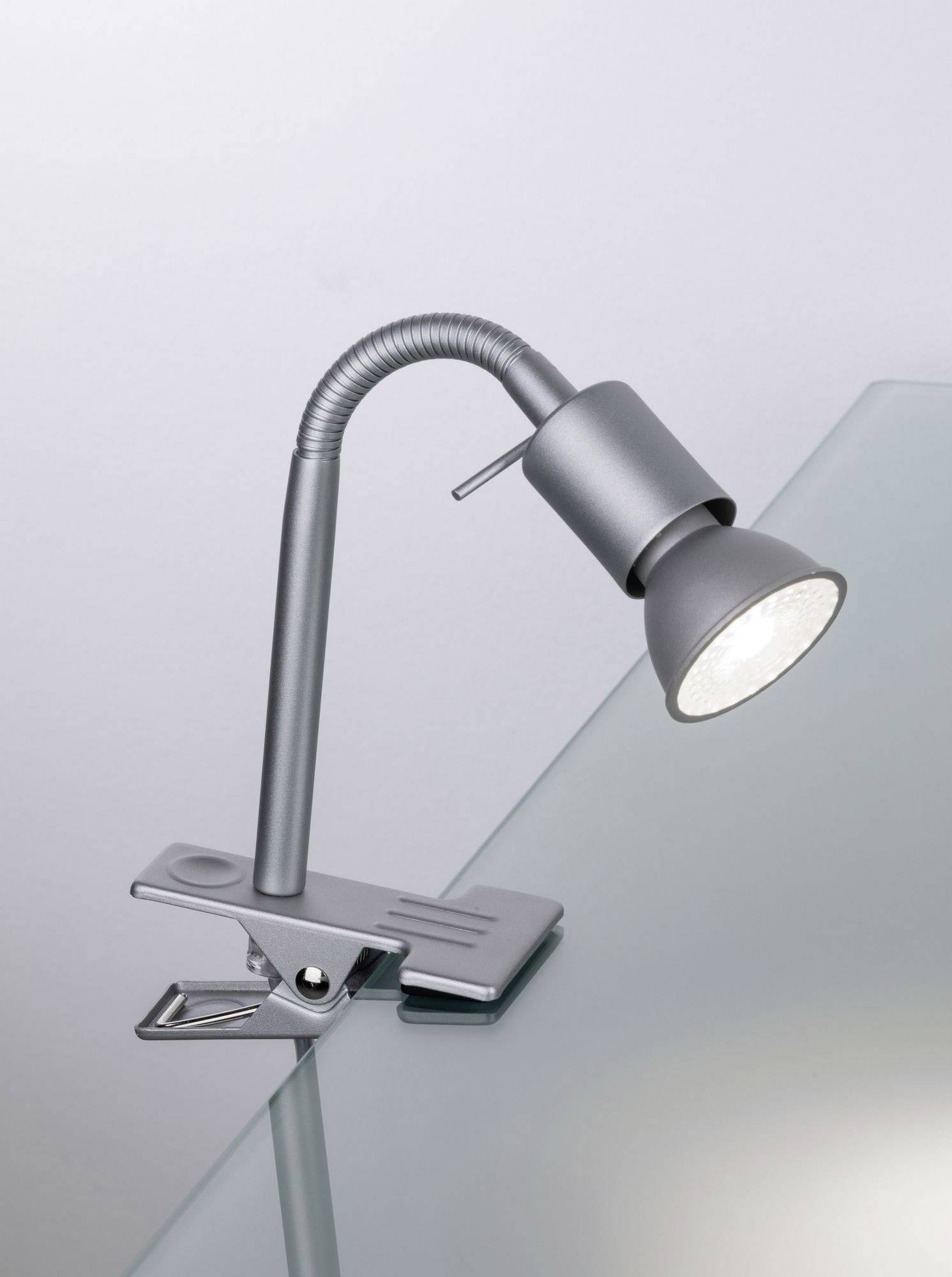 Silberne Tischlampe mit flexiblem Schwanenhals und Klemme an Glasplatte befestigt, leuchtet nach unten.