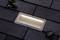 Beleuchtete Gehwegplatte in Dunkelheit, umgeben von dunklen Pflastersteinen und einigen trockenen Blättern.