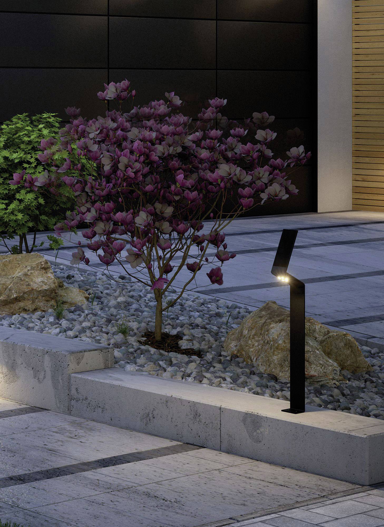 Eine modern gestaltete Terrasse mit einem beleuchteten Weg und einem Busch mit lila Blüten, umgeben von dekorativen Steinen und Felsen.