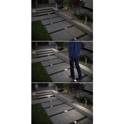 Ein beleuchteter Gehweg vor einem Haus bei Dunkelheit. Eine Person geht den Weg hinauf, wobei quadratische Lampen den Weg markieren.