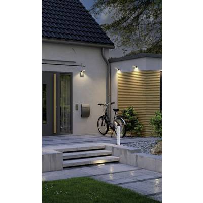Ein modernes Haus mit beleuchtetem Eingang, einer Treppe und einem Fahrrad, das an der Hauswand lehnt. Abendszene mit Garten.