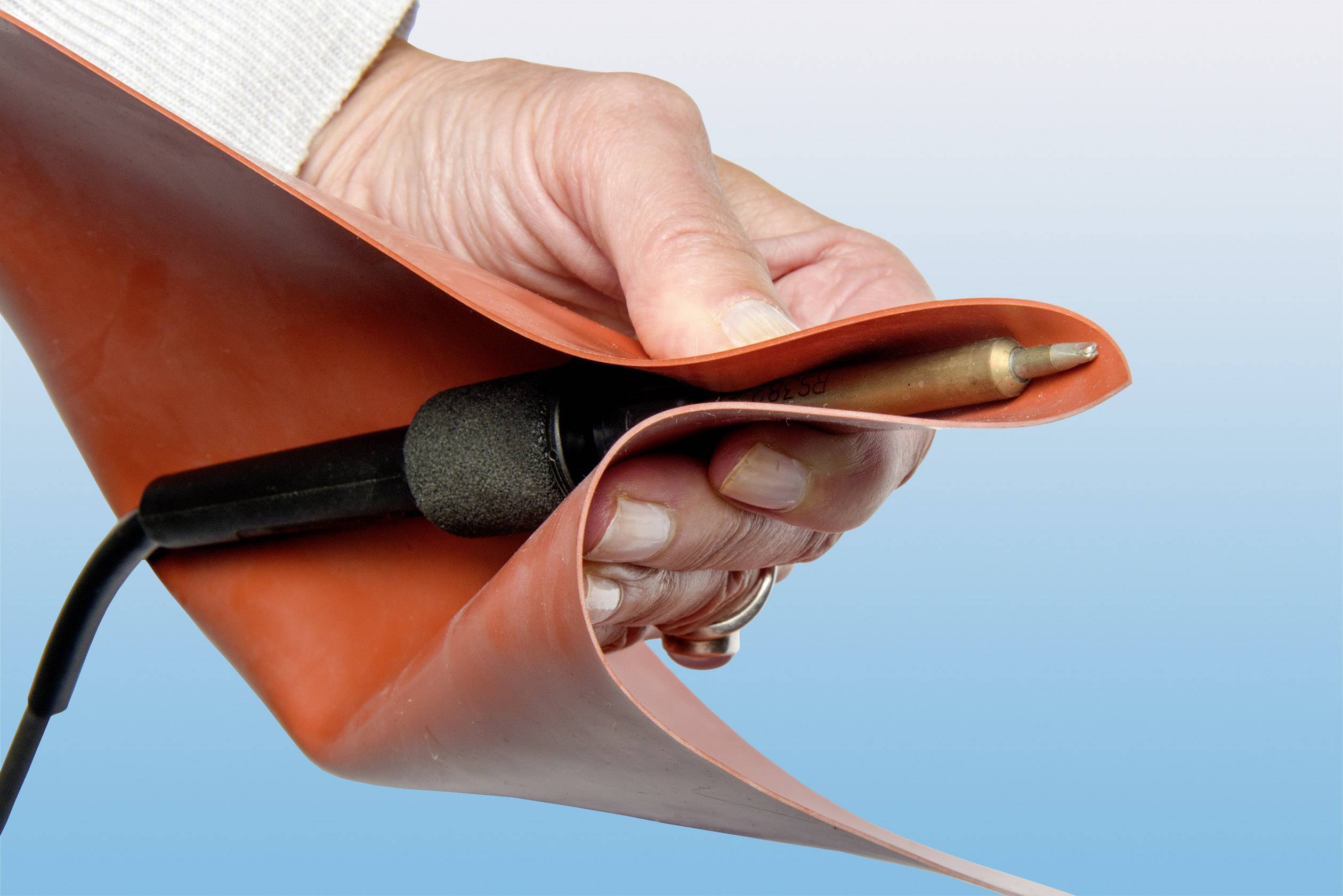 Eine Hand hält einen Lötkolben mit einem orangefarbenen Hitzeschutz, der das Werkzeug umwickelt, vor einem blauen Hintergrund.