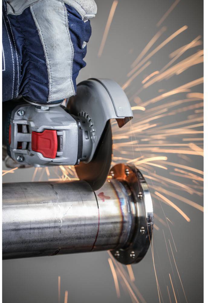 Arbeiter mit Schutzkleidung schneidet Metallrohr mit einer Trennschleifmaschine, Funken fliegen.