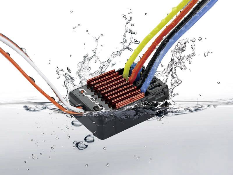 Elektronisches Bauteil mit Kabeln und Kühlrippen, teilweise unter Wasser, umgeben von Spritzwasser.