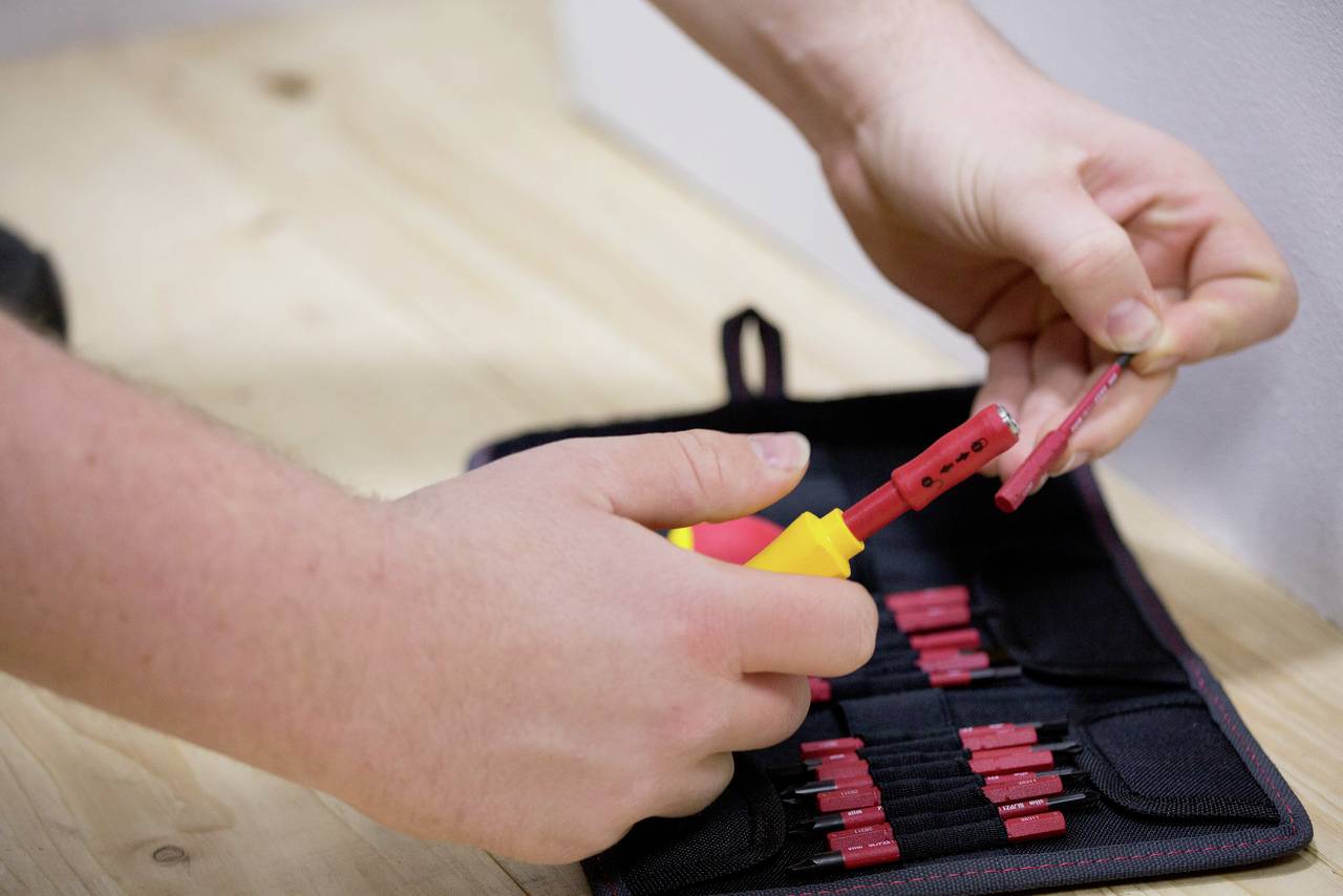 Eine Person benutzt einen Schraubendreher, um einen roten Stecker aus einer Werkzeugtasche zu montieren.