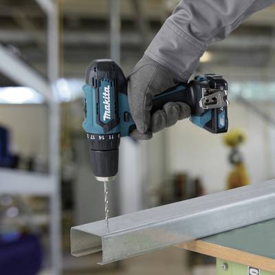 Person hält eine Bohrmaschine und bohrt ein Loch in einen Metallträger in einer Werkstattumgebung.