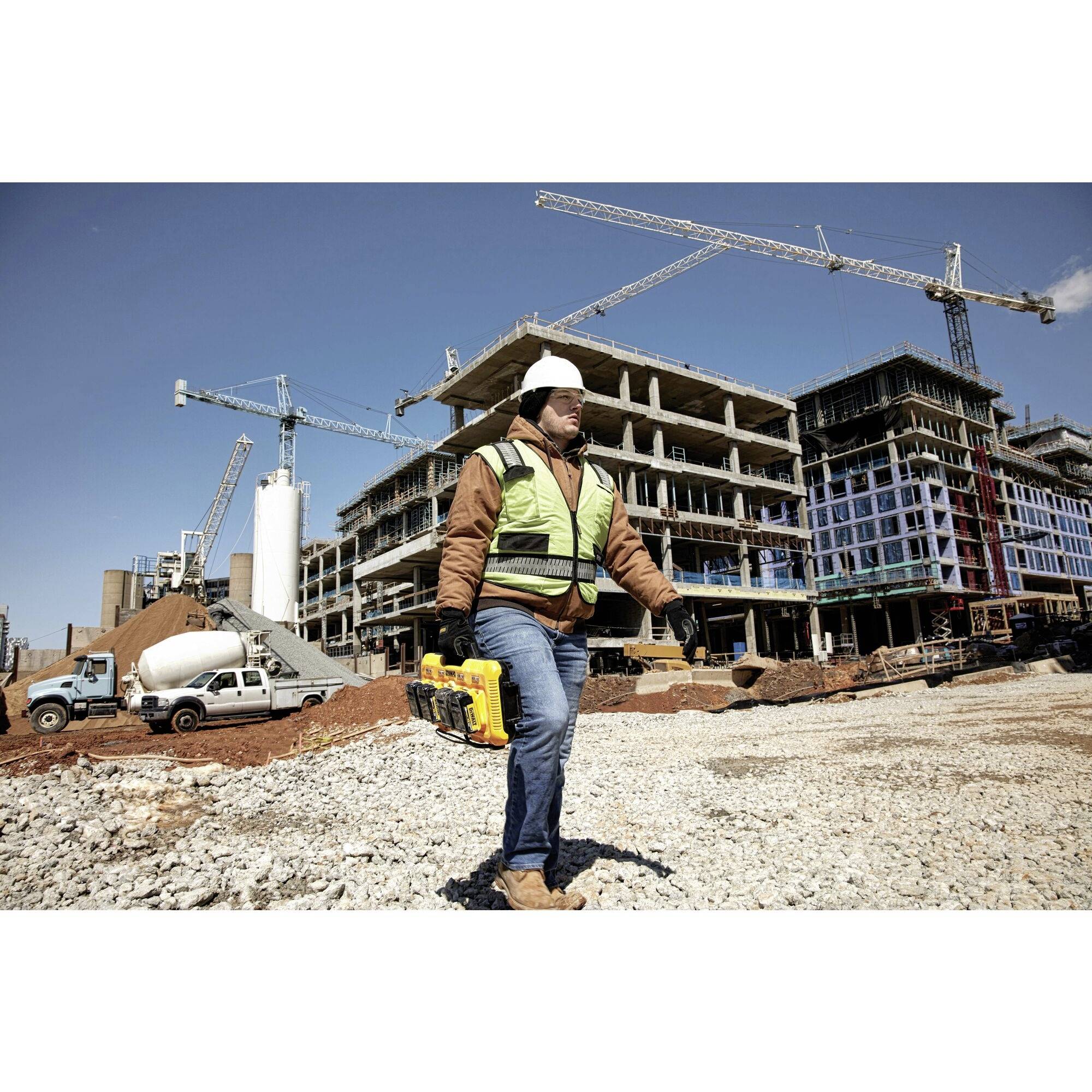 Arbeiter mit Schutzhelm und Weste steht auf Baustelle, im Hintergrund unvollendete Gebäude und Kräne.