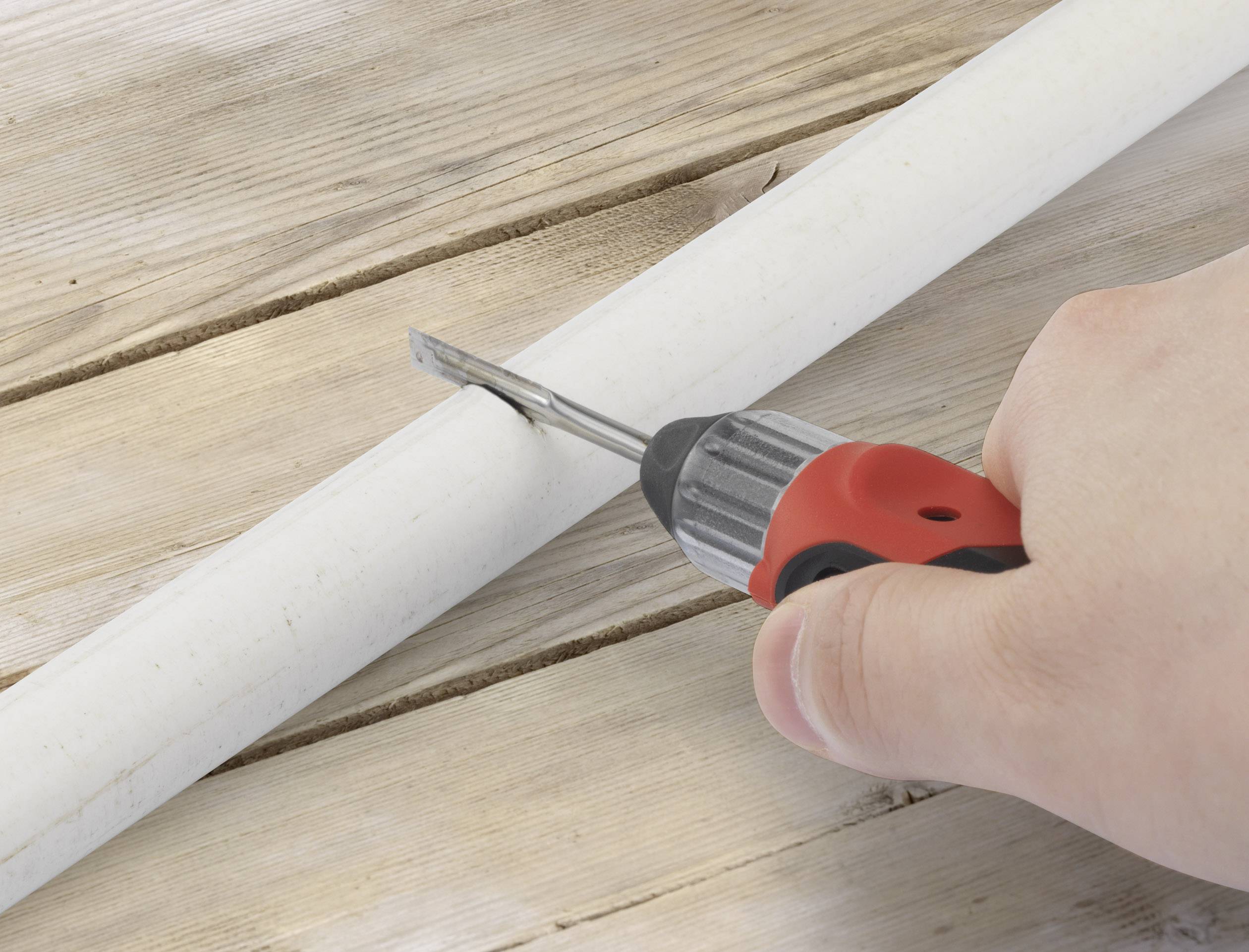 Eine Hand hält einen Schraubendreher an einem weißen Rohr auf einem Holztisch.