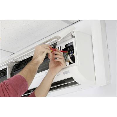Eine Person repariert eine Klimaanlage an der Wand. Hände mit Schraubendreher arbeiten im Inneren des Geräts.