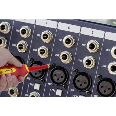 Eine Hand steckt einen roten Schraubenzieher in einen Mikroeingang an einem Audiopanel mit mehreren Buchsen und Beschriftungen.