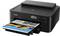 Ein schwarzer Canon-Drucker druckt ein farbiges Foto, sichtbar in der Papierablage. Der Drucker hat Bedienknöpfe und ein Display.