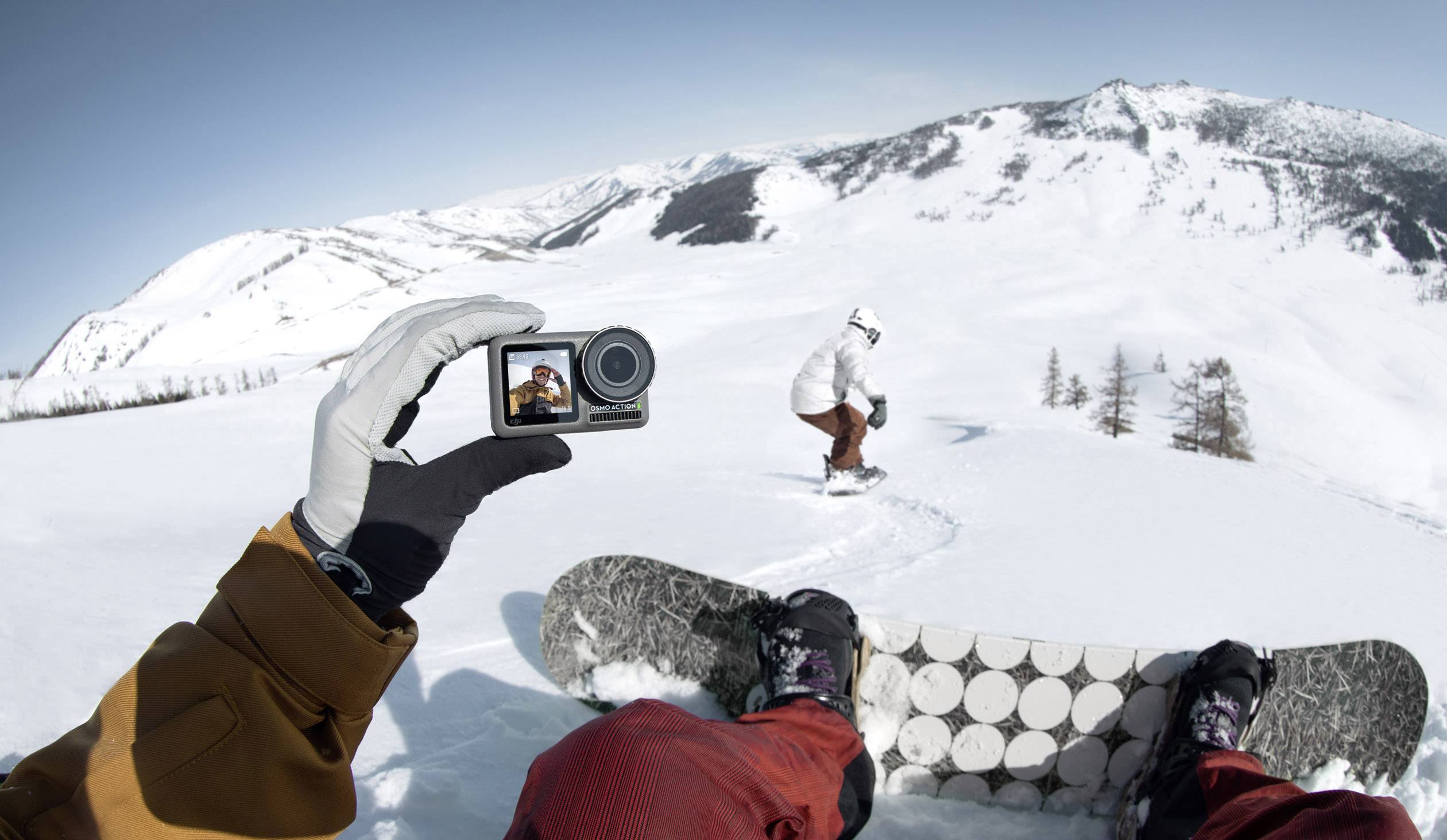 Person fährt snowboard in schneebedeckten Bergen, während jemand die Szene mit einer kleinen Kamera aus der Ich-Perspektive filmt.