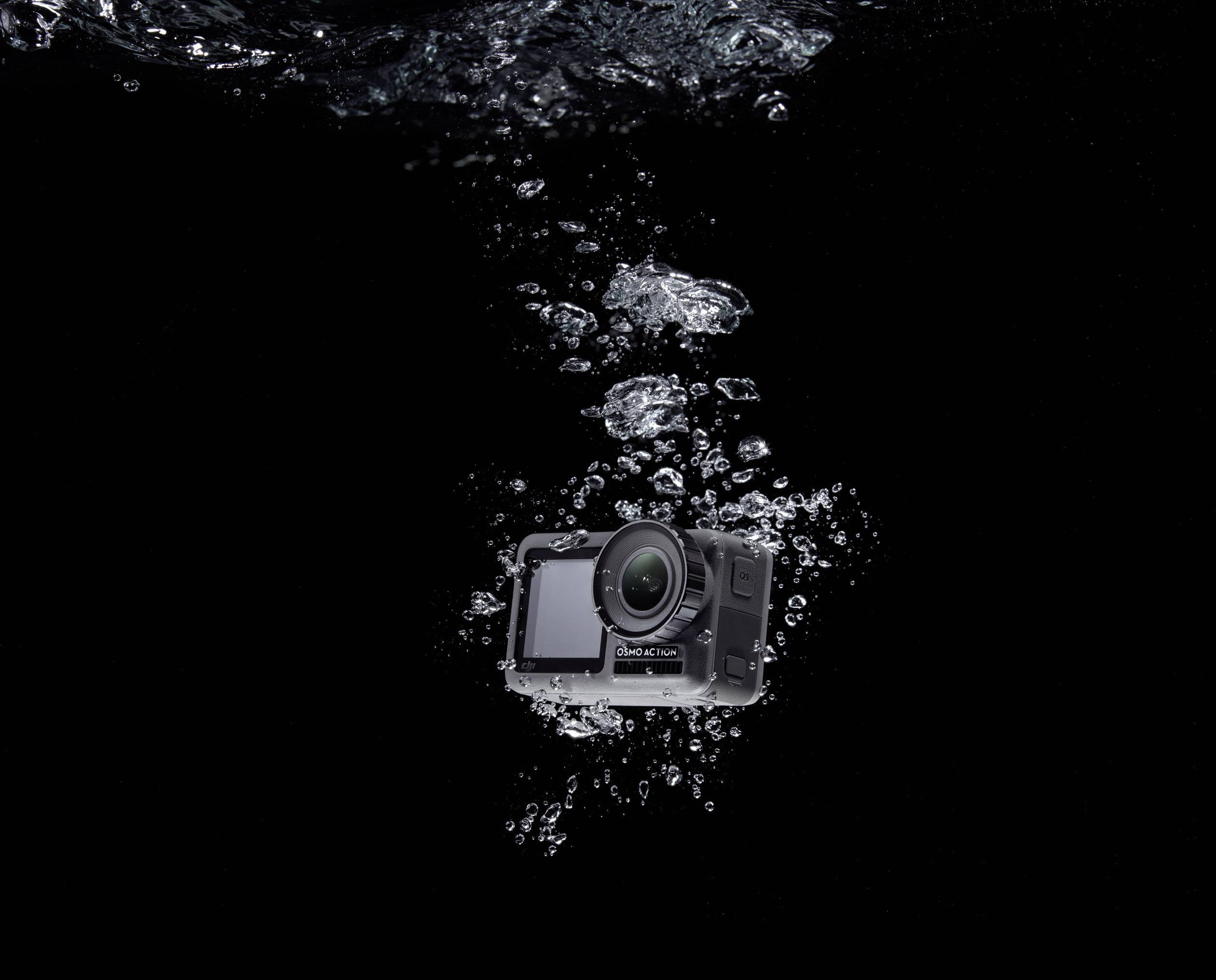 Unterwasseraufnahme einer Kamera, die in sprudelndem Wasser schwebt. Die Kamera ist zentral platziert vor einem schwarzen Hintergrund.