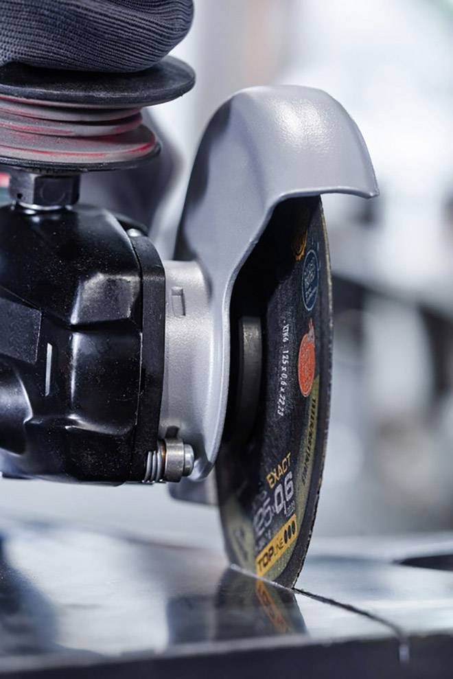 Nahaufnahme eines Winkelschleifers mit montierter Trennscheibe, während er Metall schneidet. Schutzvorrichtungen sind sichtbar.