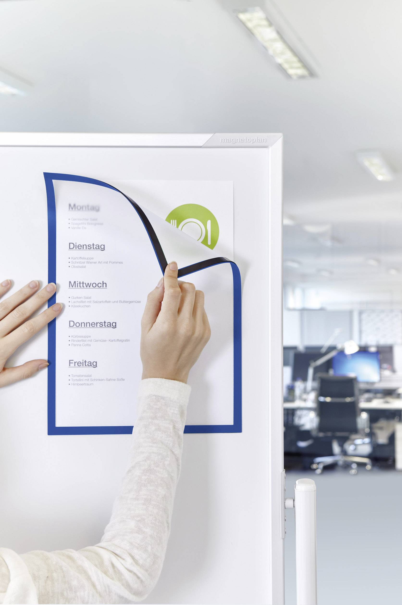 Eine Person wechselt das Kalenderblatt an einer Tafel im Büro. Der Kalender zeigt Wochentage an. Im Hintergrund ein modernes Büro.