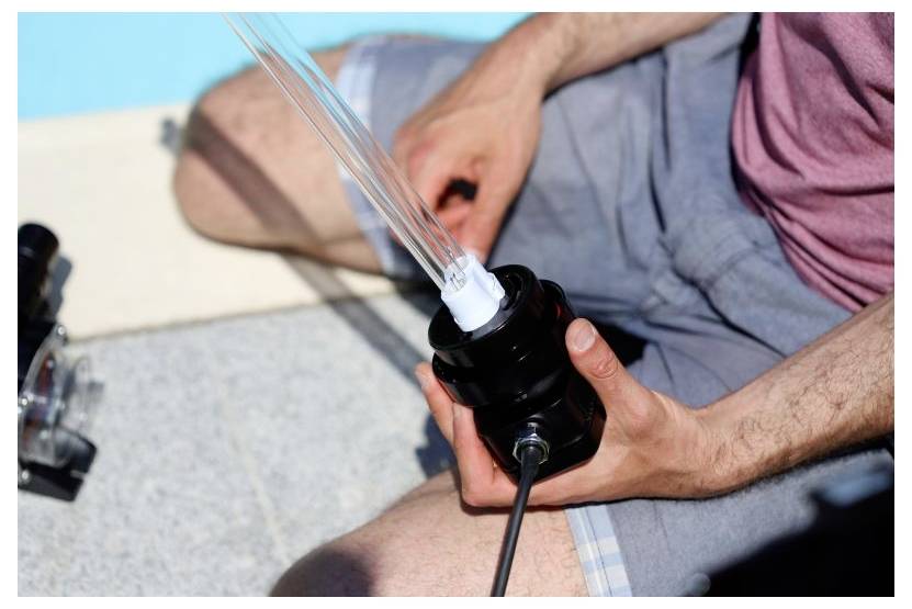 Eine Person hält eine UV-Lampen-Baugruppe und bereitet sie für die Installation oder Wartung in einem Außenbereich mit hellem Hintergrund vor.