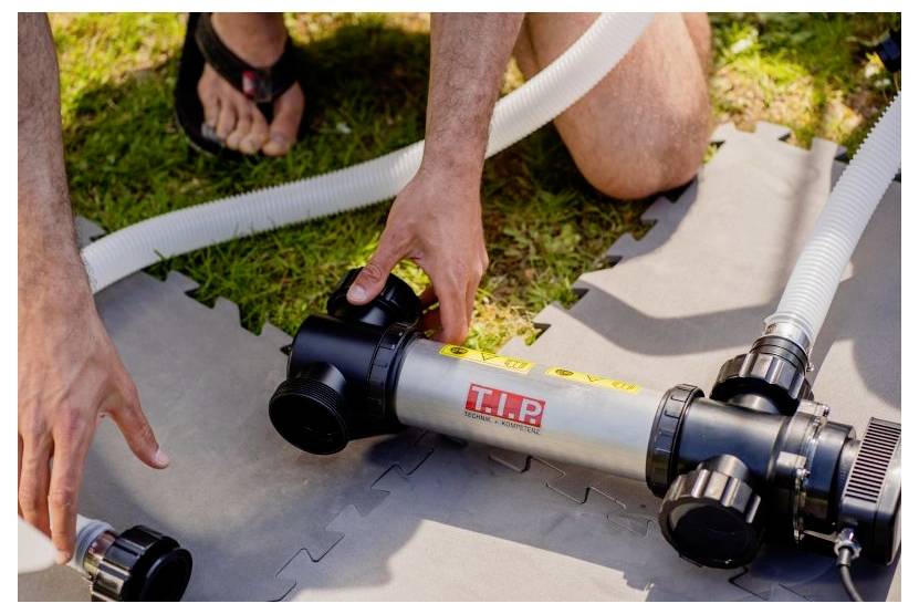 Eine Person, die eine Poolpumpe mit Schläuchen auf einer Matte im Freien zusammenbaut und die Ausrüstung sorgfältig handhabt.