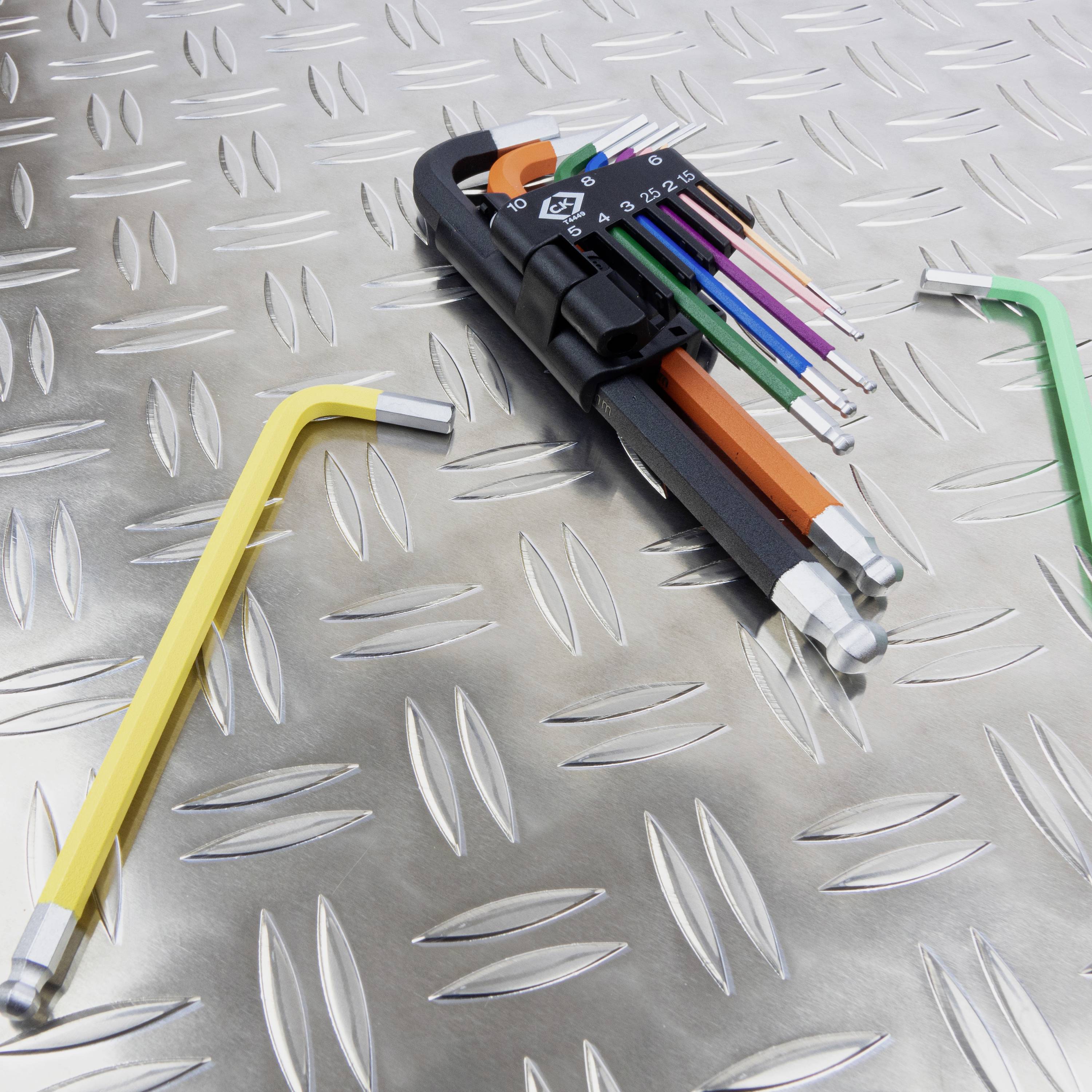 Ein Satz bunter Winkelschlüssel mit einem gelben, entnommenen Schlüssel liegt auf einer geriffelten Metalloberfläche.