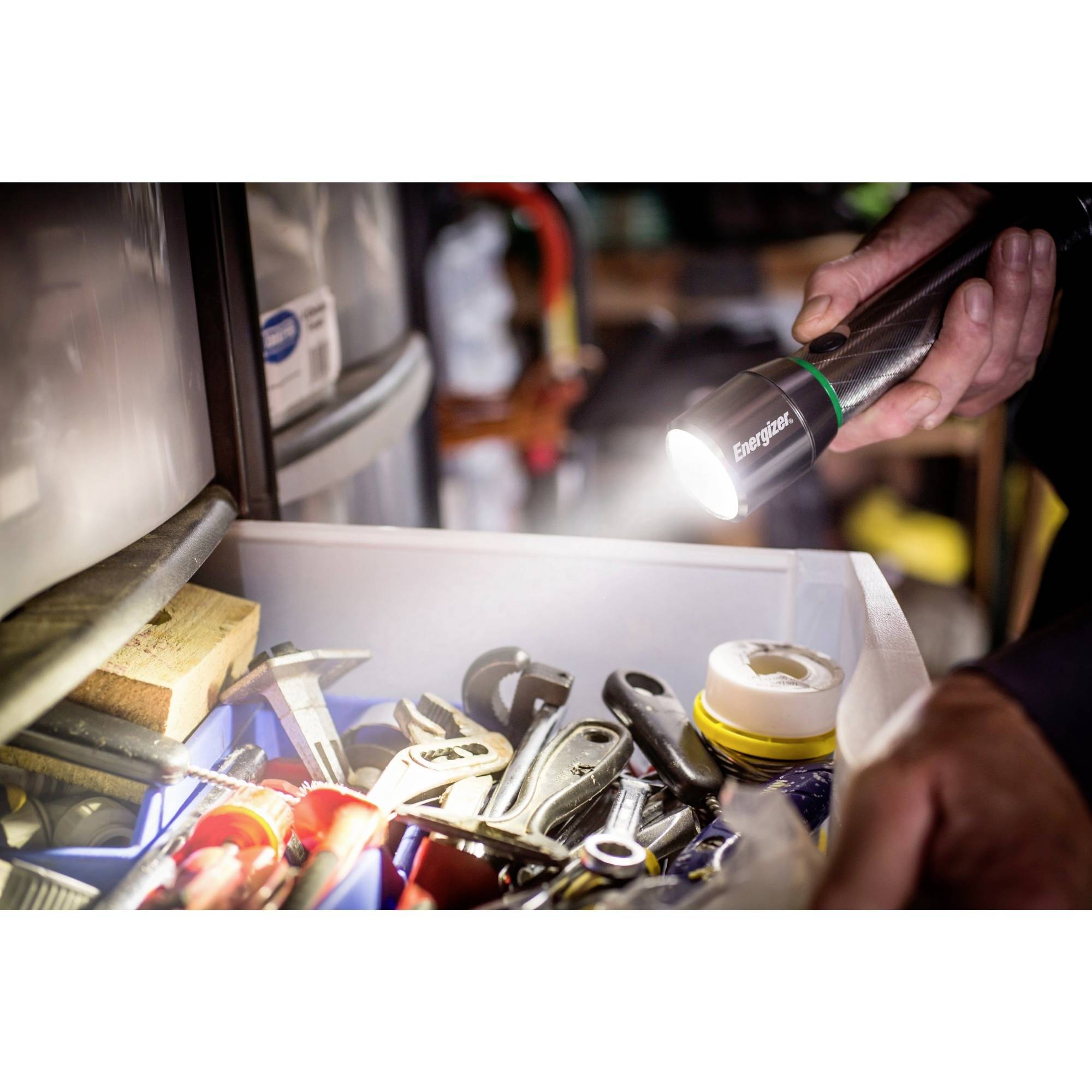 Eine Hand hält eine Taschenlampe, die in eine Schublade mit verschiedenen Werkzeugen und Materialien leuchtet.