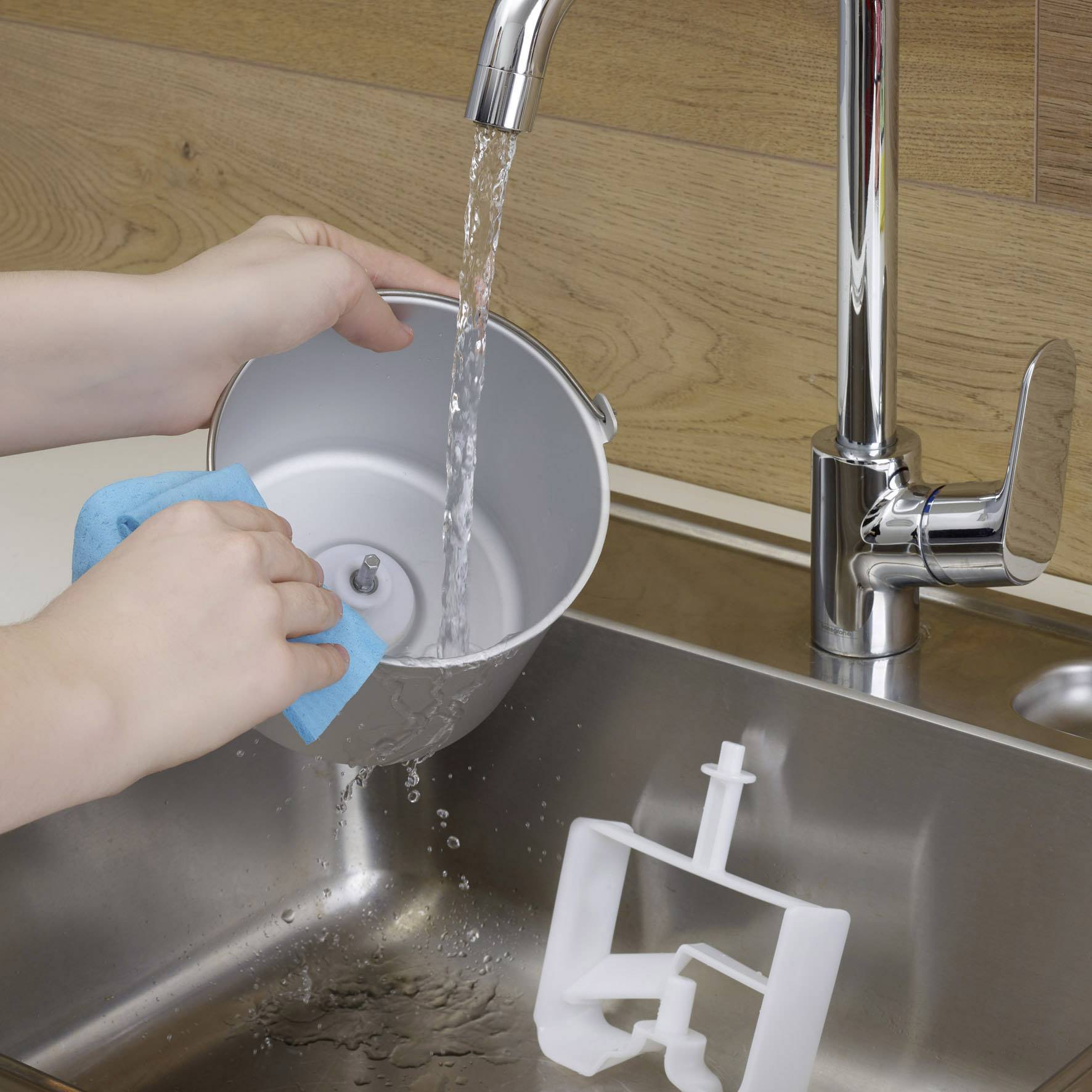 Eine Person spült einen grauen Behälter unter fließendem Wasser in der Küche ab. Ein blauer Schwamm wird verwendet.