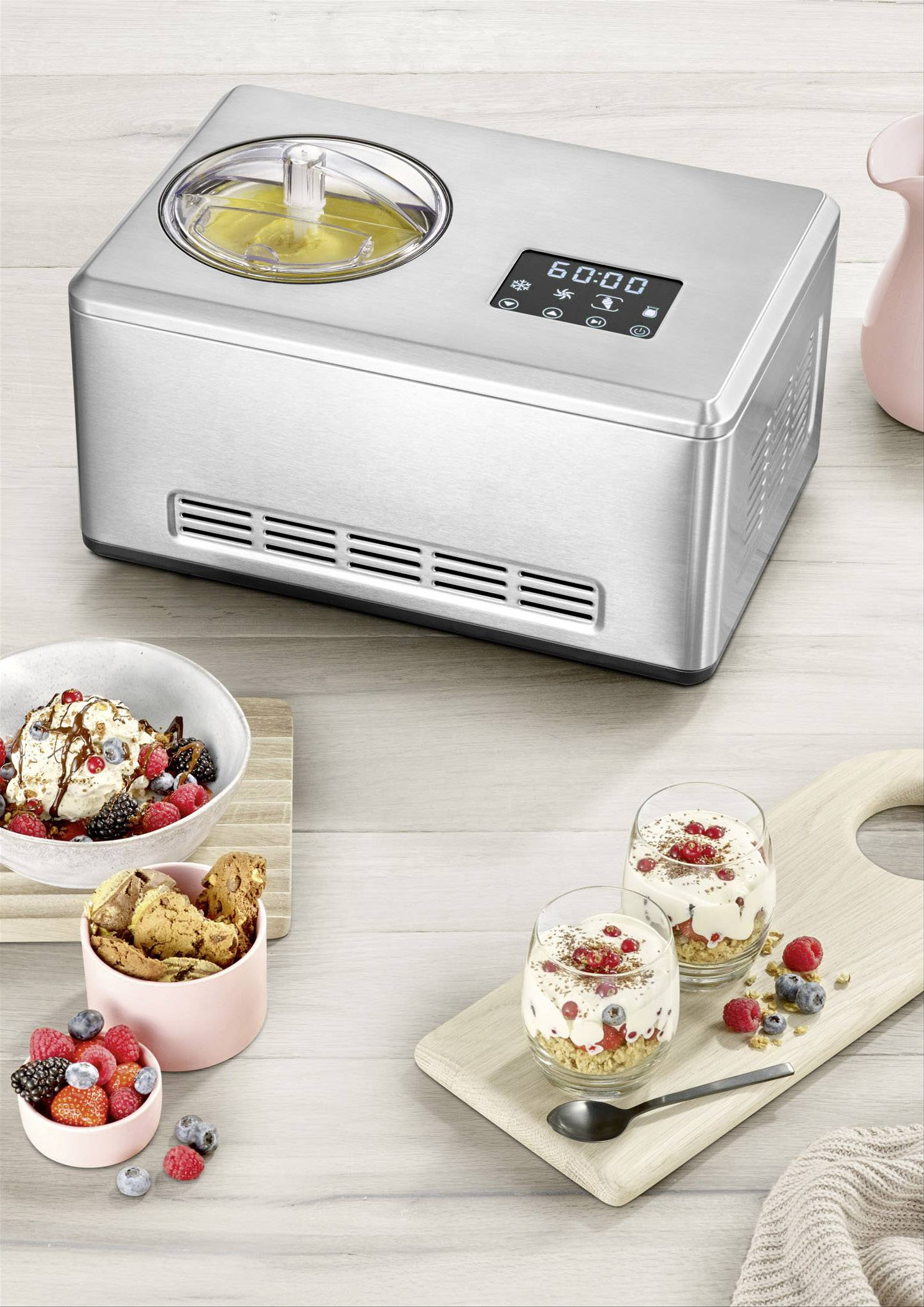 Eismaschine aus Edelstahl mit digitalem Display, daneben fertiges Eis in Schalen und Gläsern, dekoriert mit Beeren und Keksen.