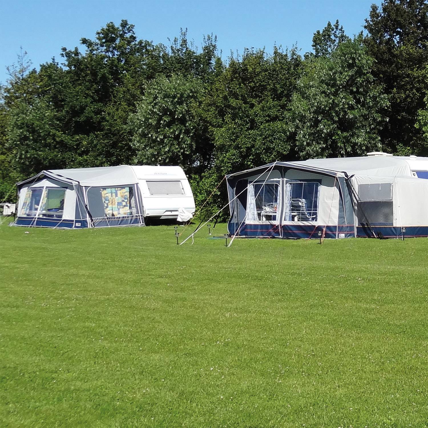 Zwei große Wohnwagen mit Vorzelten stehen auf einer grünen Wiese vor einem Hintergrund aus Bäumen, ideal für Camping.
