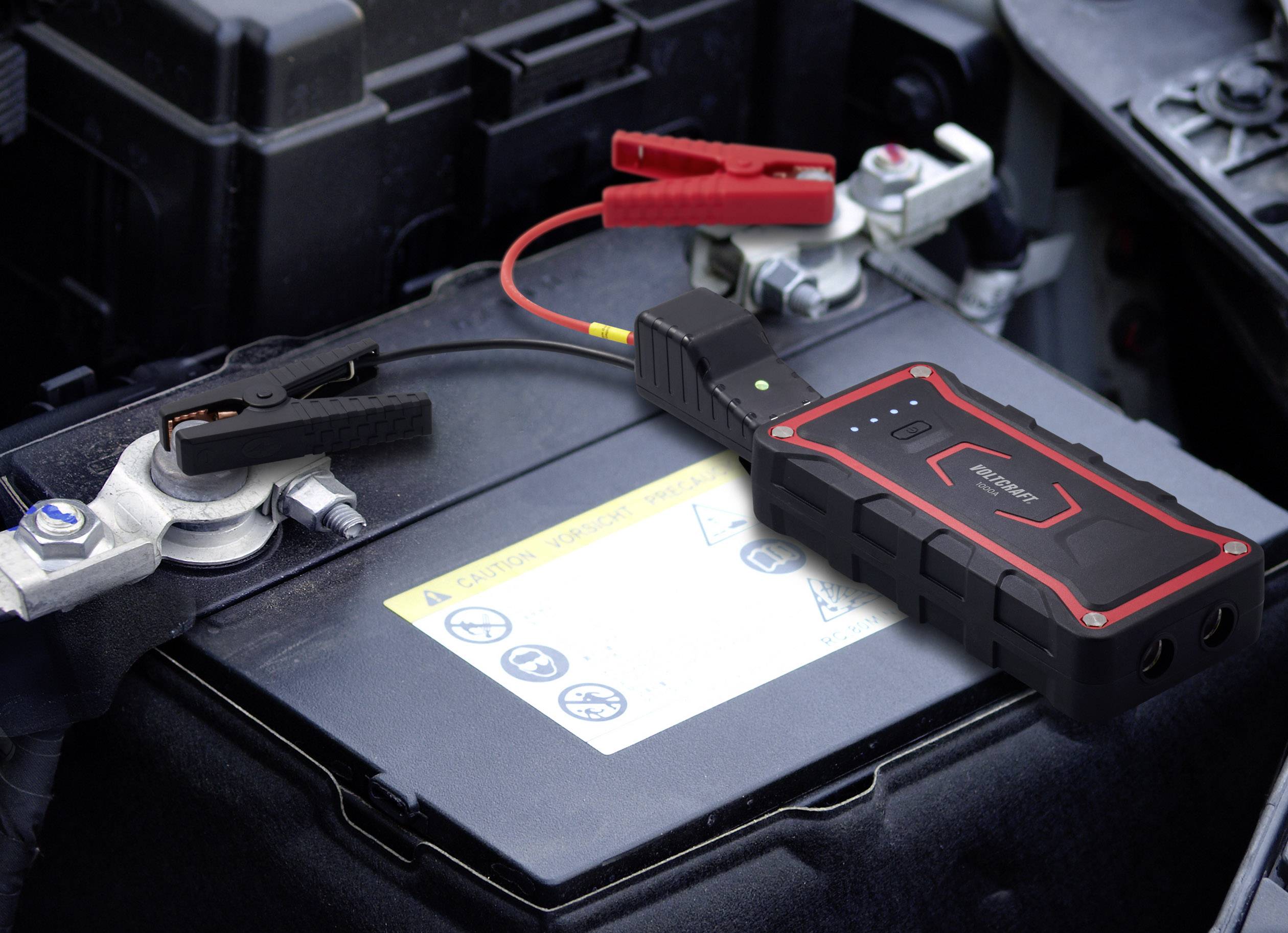 Eine Autobatterie wird von einem mobilen Starthilfegerät aufgeladen. Die Klemmen sind korrekt an den Batteriepollen angebracht.