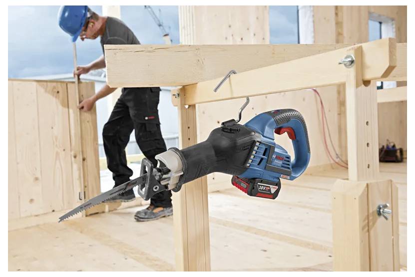 Ein Bauarbeiter in Sicherheitsausrüstung montiert Holzrahmen in einer teilweise fertiggestellten Holzkonstruktion. Eine Kreissäge ist prominent im Vordergrund platziert.