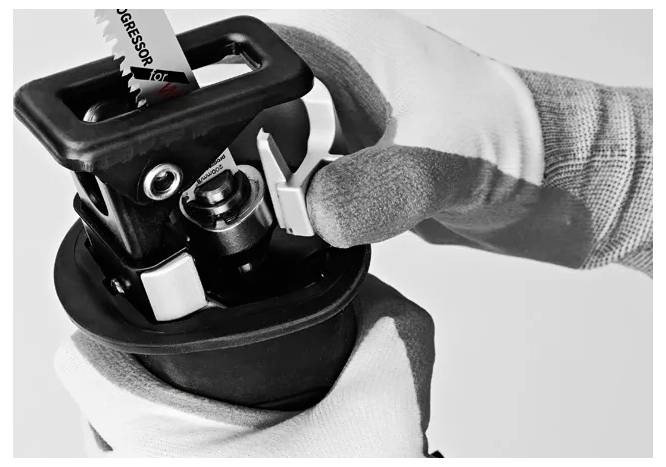 Eine Person, die Schutzhandschuhe trägt, schiebt eine Sägeblatt in ein Elektrowerkzeug und betont damit den sicheren Umgang mit Arbeitsausrüstung.