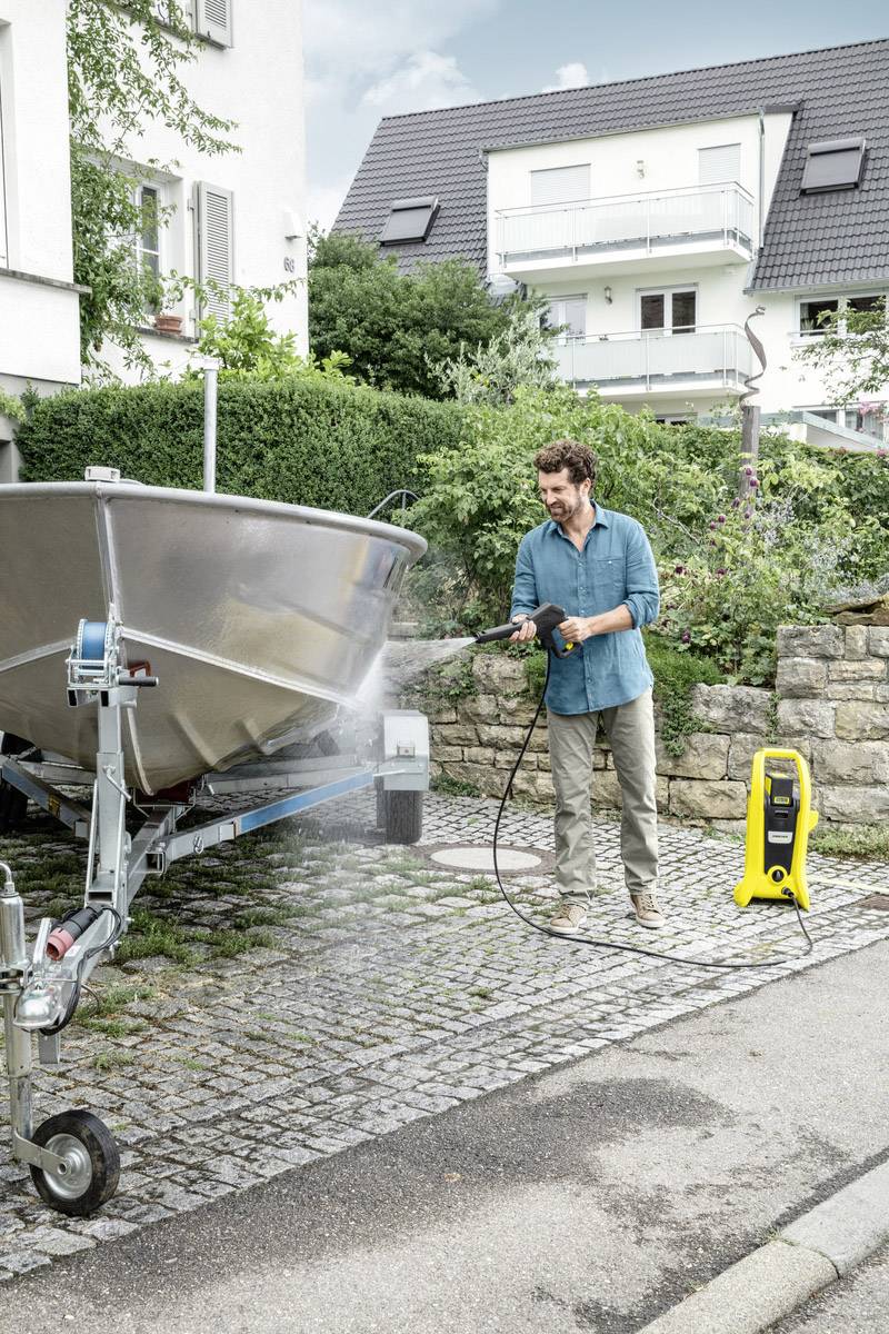 Ein Mann reinigt ein Boot auf einem Anhänger mit einem Hochdruckreiniger vor einem Wohnhaus.