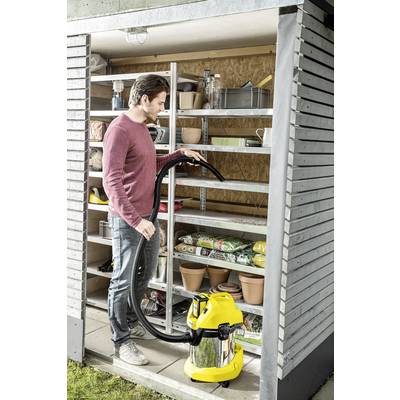 Ein Mann in einem Schuppen benutzt einen Industriestaubsauger, um den Boden zu reinigen. Auf den Regalen stehen Gartenzubehör und Töpfe.