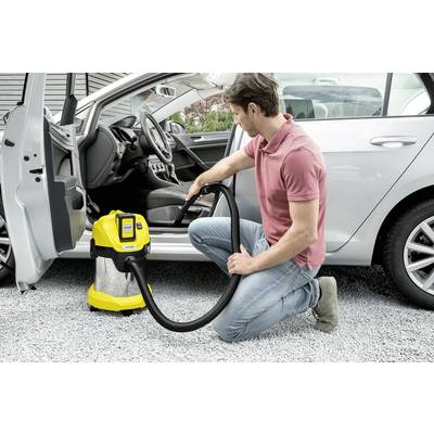 Ein Mann kniet neben einem silbernen Auto und reinigt den Innenraum mit einem gelben Staubsauger.