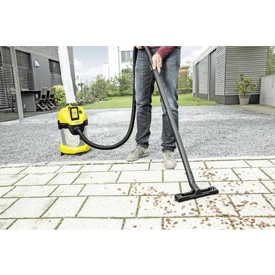 Eine Person saugt Kieselsteine von einem gepflasterten Boden mit einem gelben Industriestaubsauger ab.
