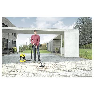 Eine Person saugt herabgefallene Blätter von einer gepflasterten Terrasse mit einem gelb-schwarzen Staubsauger in der Einfahrt eines modernen Hauses.