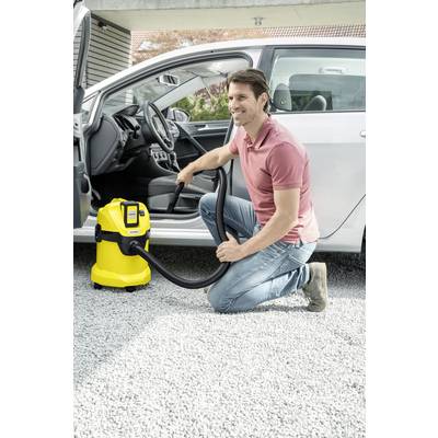 Ein Mann kniet neben einem silbernen Auto und benutzt einen gelben Industriestaubsauger, um den Innenraum zu reinigen.