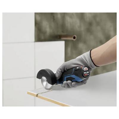 Mit Handschuh bekleidete Hand, die einen kabellosen Rotationsmesser verwendet, um eine weiße Fliese oder Platte auf einer Arbeitsfläche zu schneiden.