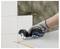 Mit Handschuh bekleidete Hand, die einen kabellosen Rotationsmesser verwendet, um eine weiße Fliese oder Platte auf einer Arbeitsfläche zu schneiden.