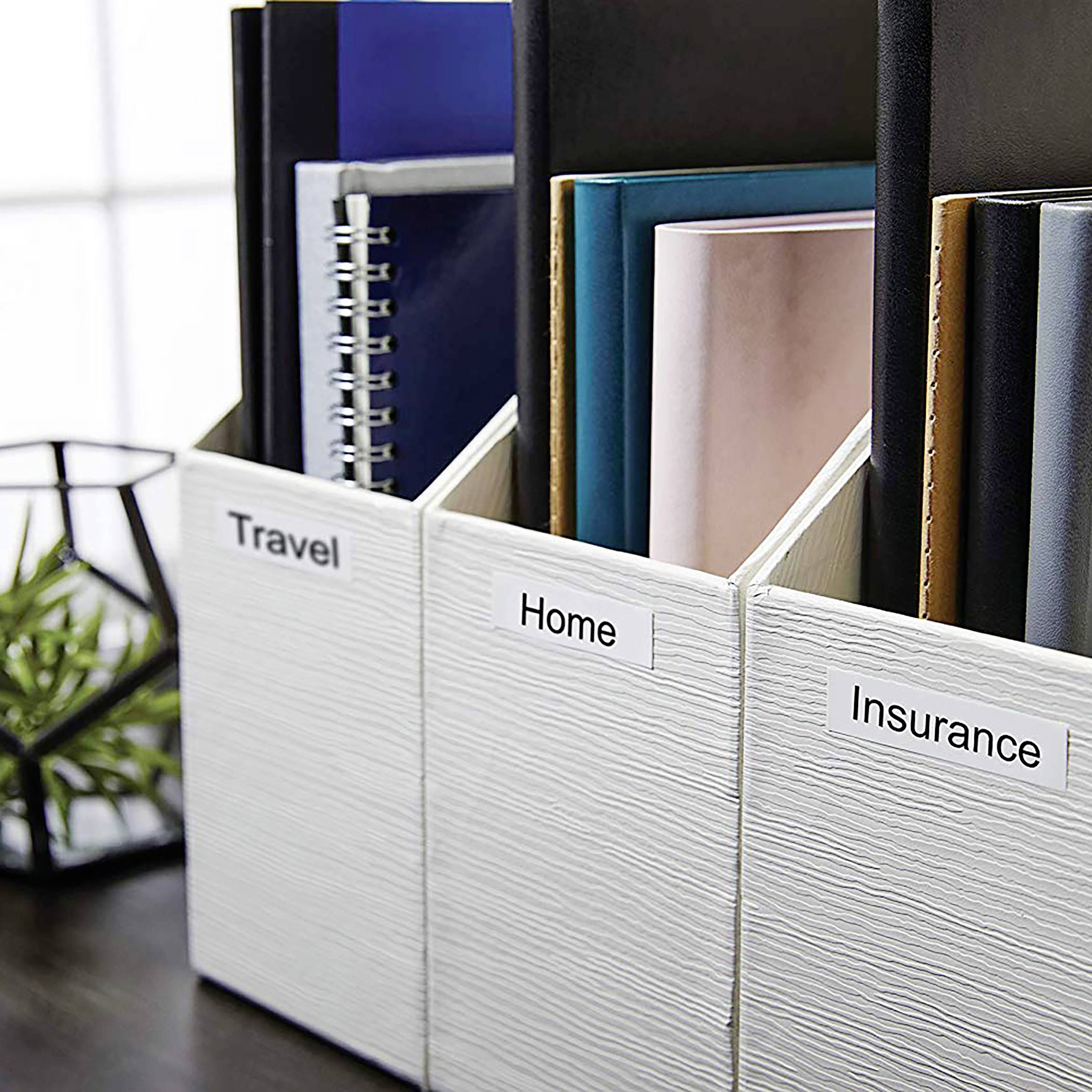 Drei weiße Ordner mit Etiketten: 'Travel', 'Home', 'Insurance', auf einem Regal. Links ein Pflanzenhalter, im Hintergrund ein Fenster.