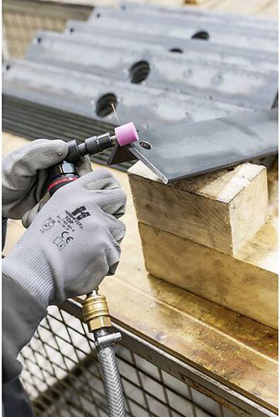 Person, die Metallplatten mit einem Brenner schweißt und Schutzhandschuhe trägt. Die Platten sind auf Holzblöcken gestapelt, mit einem Metallgitter darunter.