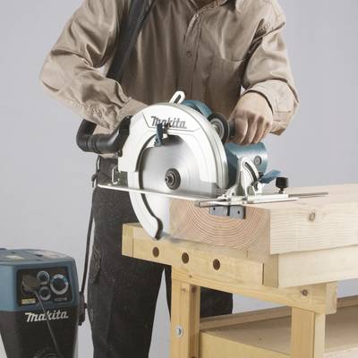 Eine Person bedient eine Kreissäge, um ein Stück Holz zu schneiden. Die Säge ist auf einem stabilen Holztisch befestigt.