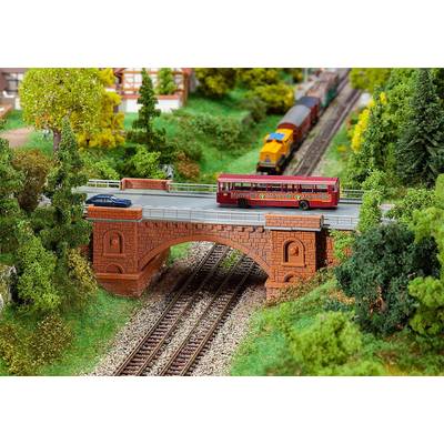 Eine Miniatureisenbahnlandschaft zeigt eine rote Brücke über Bahngleise, auf der ein roter Bus und ein Auto fahren. Darunter fährt ein Zug.