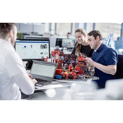 Drei Personen arbeiten gemeinsam an einem Tisch an einem technischen Projekt mit Laptops. Im Hintergrund sind Bildschirme sichtbar.