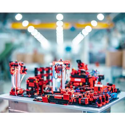 Eine Miniatur-Fabrik aus roten Bausteinen zeigt komplexe Maschinen und Roboterarme in einem hell erleuchteten Arbeitsumfeld.