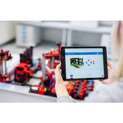 Eine Person hält ein Tablet mit einer technischen Zeichnung. Im Hintergrund befindet sich ein Modell aus roten Bausteinen.