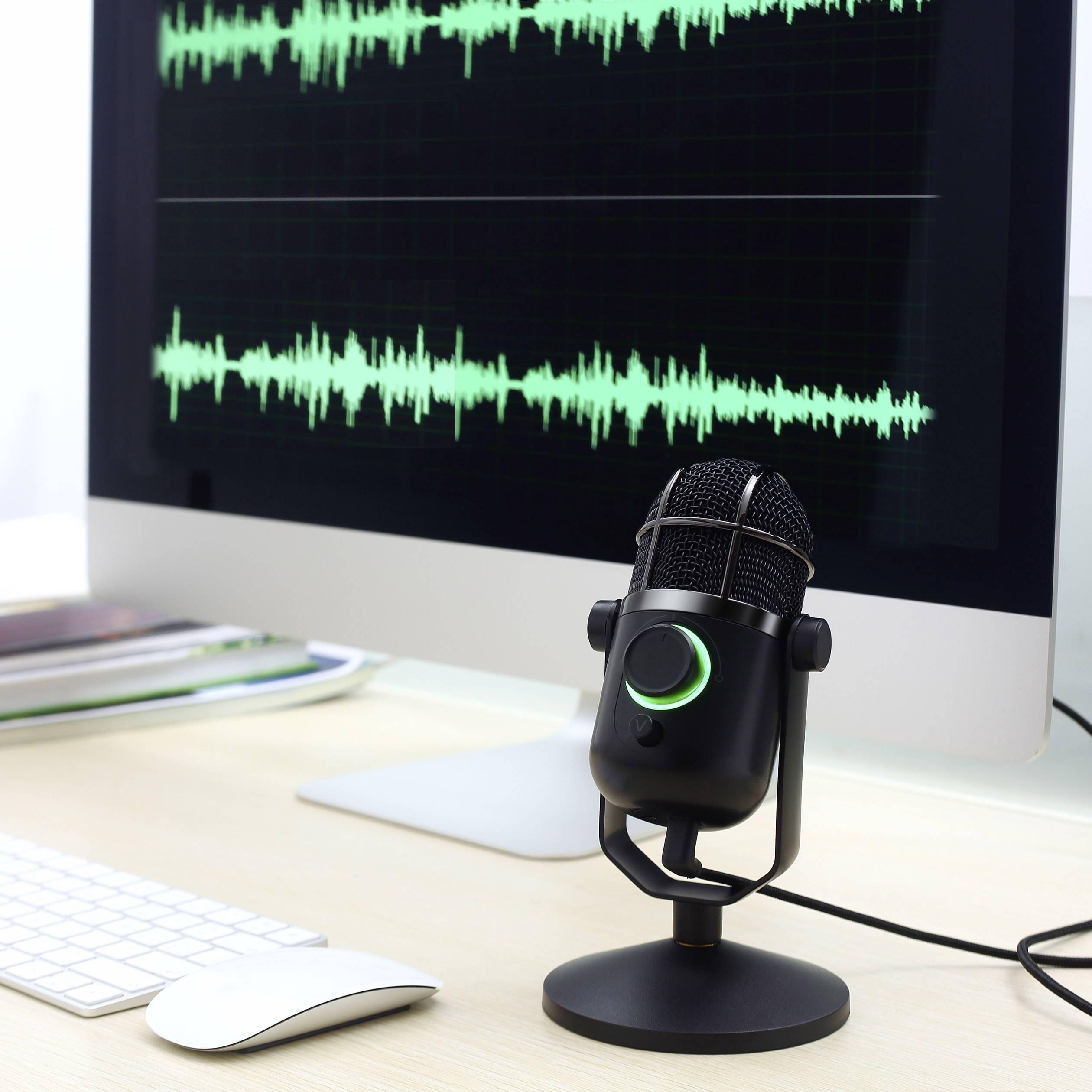 Ein Computerbildschirm zeigt eine grüne Audio-Wellenform. Ein Mikrofon steht auf einem Schreibtisch vor dem Bildschirm.